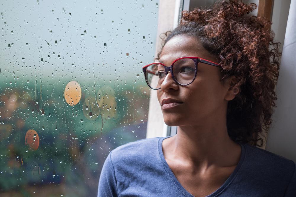 Woman stares out the rainy window, contemplating contacting a pain and suffering lawyer. 